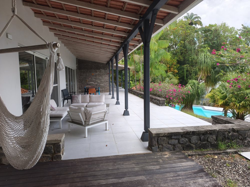 Grande terrasse couverte ouverte sur le jardin et la piscine, en Martinique